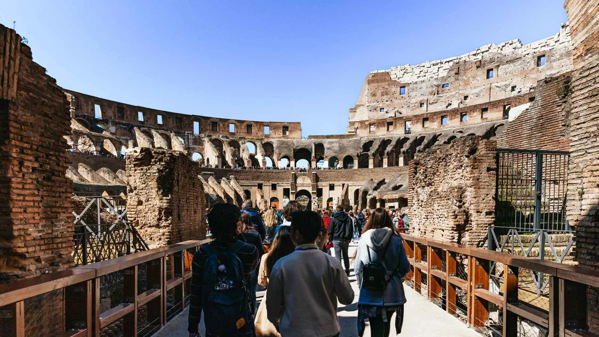 Guided group standing on the reconstructed arena floor of the Colosseum with the hypogeum visible behind them in Rome